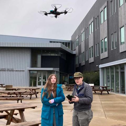 two students outside controlling a drone in flight