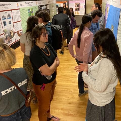 student standing by research poster explaining research to attendee at showcase event